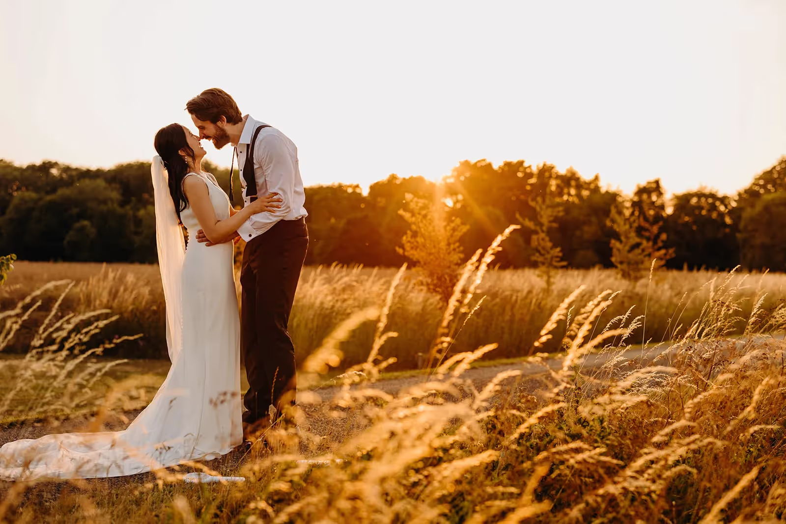 Bride and groom hug a sun sets, golden tall grass highlights in the foreground