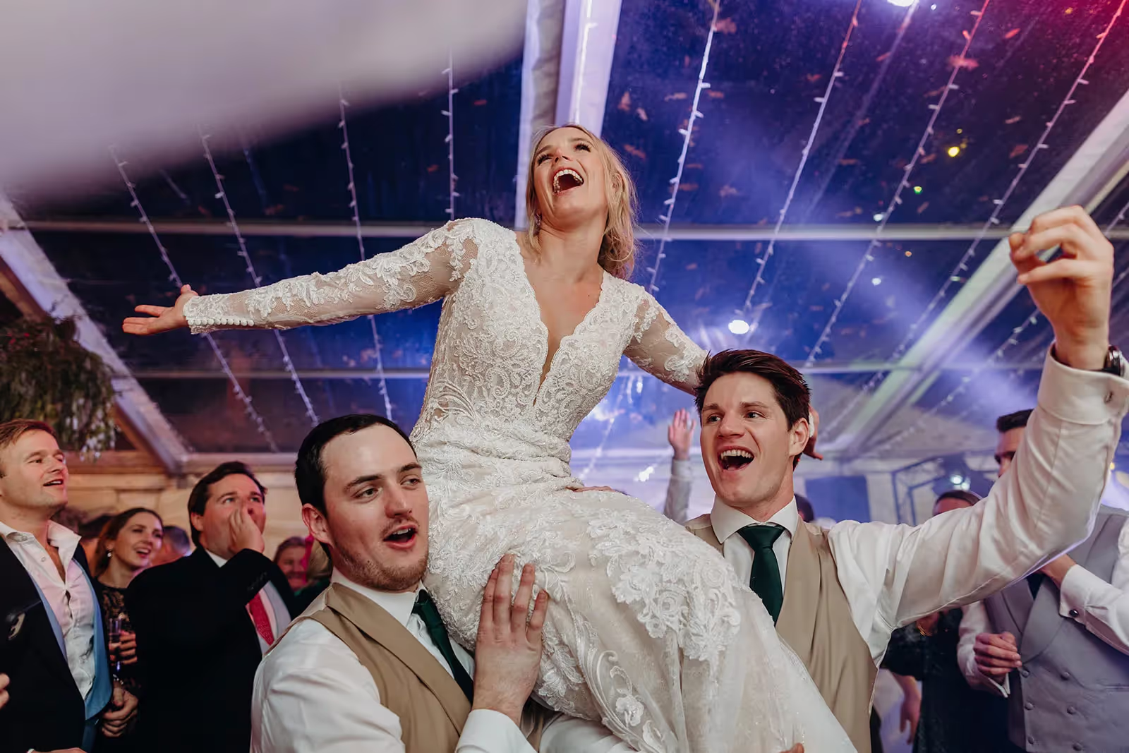 Bride being lifted up on shoulders at marquee wedding
