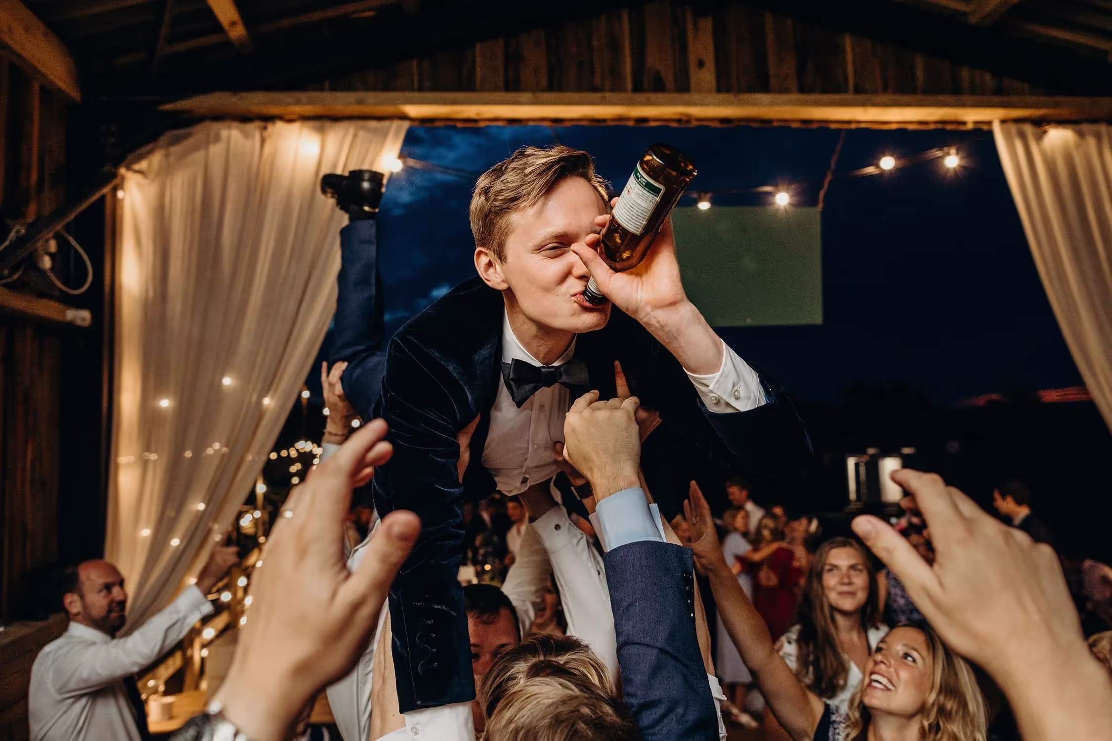 Groom being picked up in the air on dancefloor whilst drinking beer
