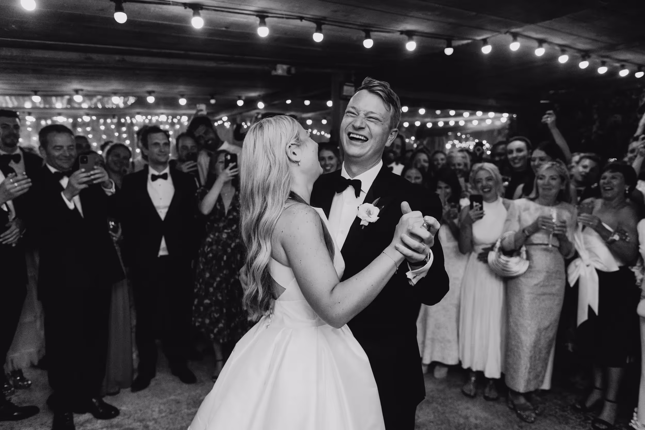 b&w of bride and groom first dance with guests blurred in background