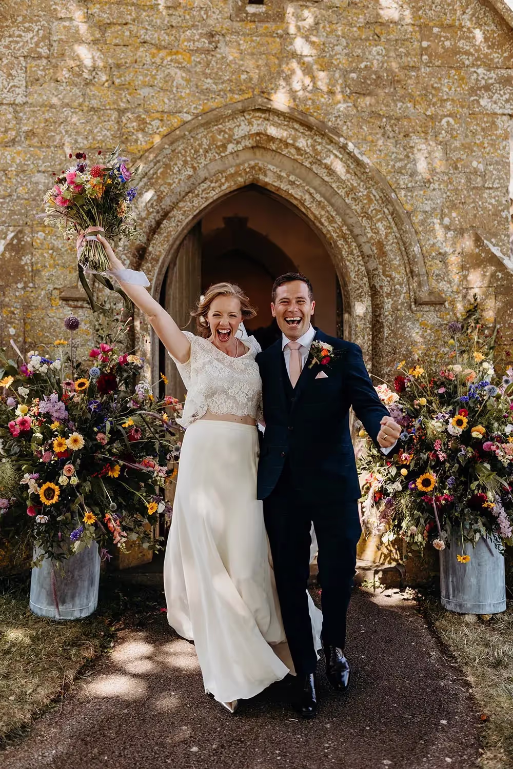 Bride and groom leaving church after just getting married, bride holds bouquet in the air and both smile