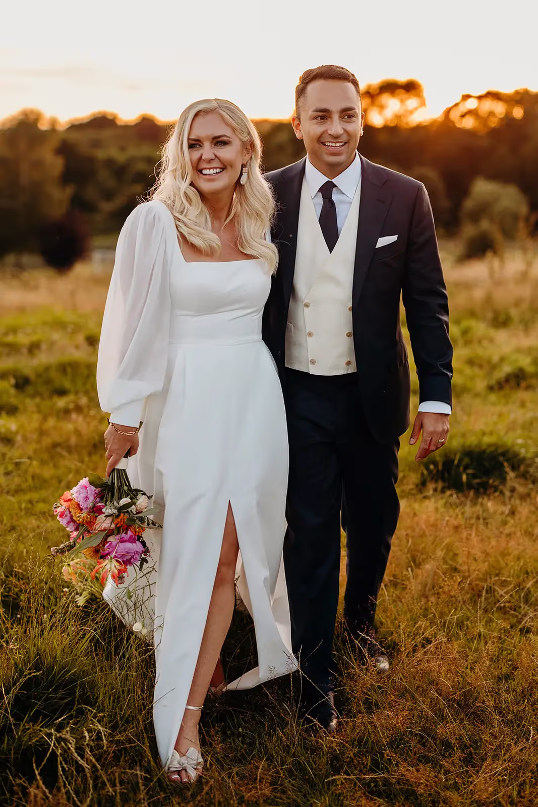 Bride and groom smiling walking along field at sunset at Surrey wedding