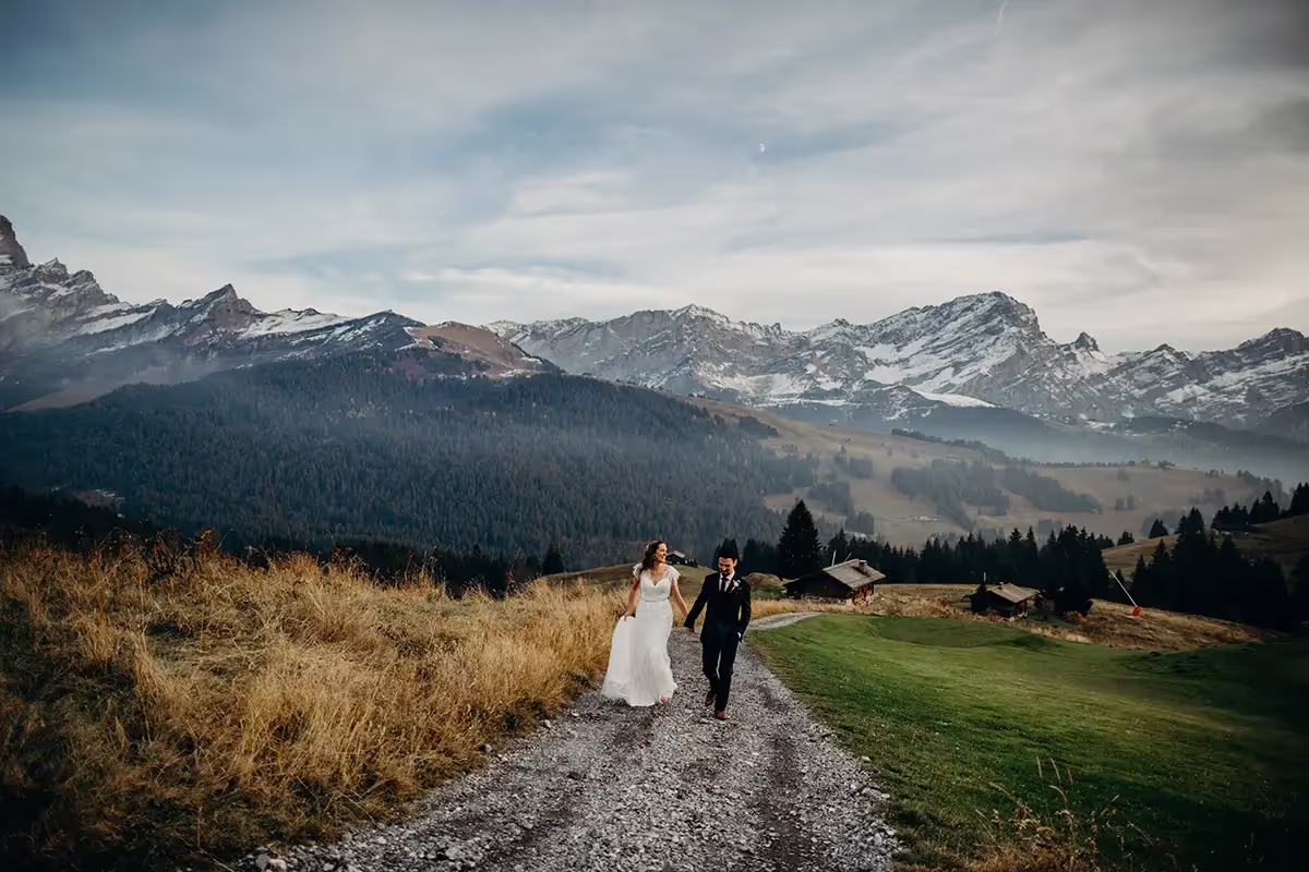 Bride and groom walk down gravel road with Swiss alps in background at Destination wedding